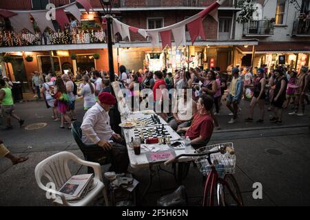 Schachmeister Jude Acers spielt ein Spiel auf der Decatur Street im French Quarter, während eine Parade vorbeizieht und den lebendigen Geist von New Orleans fängt. Stockfoto