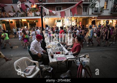 Schachmeister Jude Acers spielt ein Spiel auf der Decatur Street im French Quarter, während eine Parade vorbeizieht und den lebendigen Geist von New Orleans fängt. Stockfoto