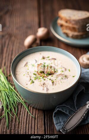 Köstliches Mittagessen, beruhigende Pilzsuppe mit frisch gehacktem Schnittlauch, serviert mit knusprigem Brot auf rustikalem Holzhintergrund Stockfoto