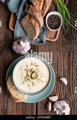 Köstliches Mittagessen, beruhigende Pilzsuppe mit frisch gehacktem Schnittlauch, serviert mit knusprigem Brot auf rustikalem Holzhintergrund Stockfoto