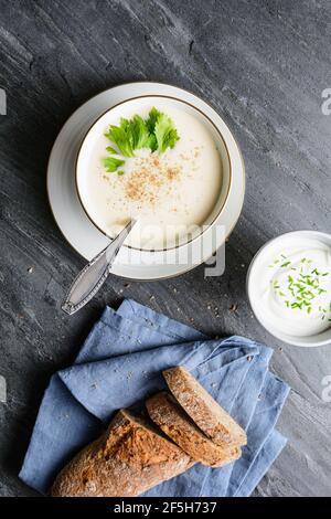 Köstliche cremige Sellerie-Suppe mit schwarzem Pfeffer und frischen Blättern, serviert mit knusprigem Brot, auf rustikalem Stein Hintergrund Stockfoto