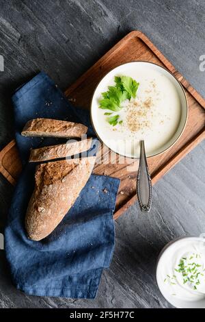 Köstliche cremige Sellerie-Suppe mit schwarzem Pfeffer und frischen Blättern, serviert mit knusprigem Brot, auf rustikalem Stein Hintergrund Stockfoto