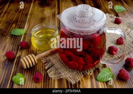 Heißer Tee mit Himbeeren, Honig und Minze auf dem rustikalen Holzhintergrund. Gesundes Getränk. Stockfoto