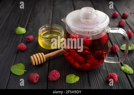 Heißer Tee mit Himbeeren, Honig und Minze auf dem schwarzen Holzhintergrund. Gesundes Getränk. Stockfoto