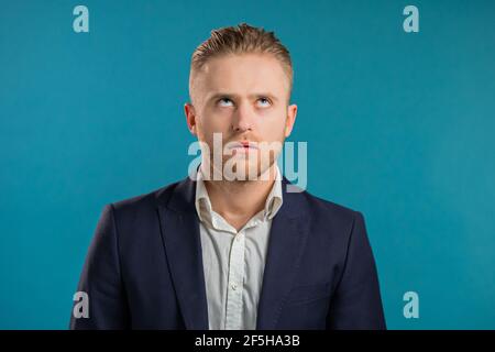 Irritierter Geschäftsmann seufzt, rollende Augen auf blauem Hintergrund. Europäischer Kerl in Unmut, er ist der Situation müde, denkt, wie kann man noch nicht Stockfoto