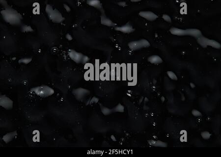 Spritzer und Tropfen auf die Oberfläche der Flüssigkeit. Abstrakter Schwarzer Hintergrund Flüssige Textur. Stockfoto