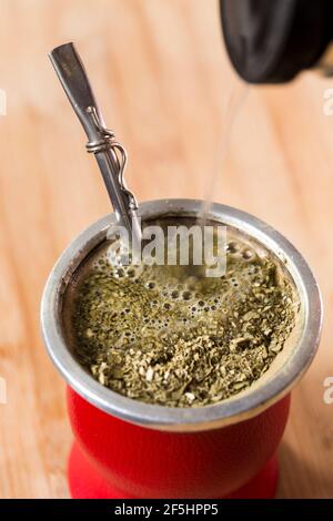 Vertikale Nahaufnahme Von Hot Traditional South American, Caffein-Reiches Drink Mate (Yerba Mate) In Red Gourd. Thermoskanne Mit Wasser Stockfoto