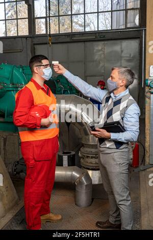 Mann verwendet Infrarot-Stirnthermometer am Arbeitsplatz während einer COVID-19 Pandemie. Stockfoto