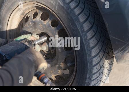 Ersetzen eines Rades an einem Auto. Schrauben am Rad lösen. Hände in alten Handschuhen. Stockfoto