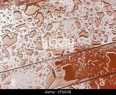 Regen Wassertropfen auf roten Holz diagonalen Textur Möbel im Freien roten Hintergrund Bild. Regenwassertropfen auf einer roten Bank Stockfoto