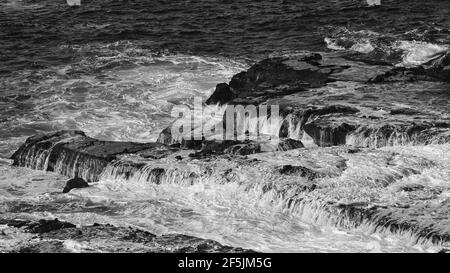Wellen laufen von flachen schwarzen vulkanischen Felsen auf einem stürmischen Tag Stockfoto
