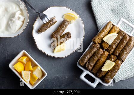 Yaprak sarmasi ist ein traditionelles türkisches Gericht, das durch das Einwickeln von Reisfüllung mit Traubenblättern hergestellt wird. Serviert in Porzellanteller mit Zitronenscheiben und einer Tasse Stockfoto