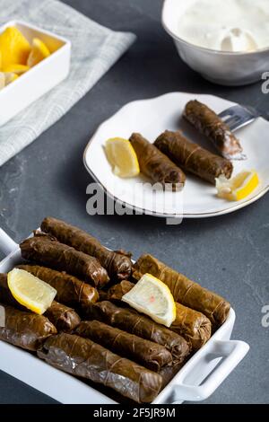 Yaprak sarmasi ist ein traditionelles türkisches Gericht, das durch das Einwickeln von Reisfüllung mit Traubenblättern hergestellt wird. Serviert in Porzellanteller mit Zitronenscheiben und einer Tasse Stockfoto