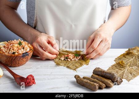 Yaprak sarmasi ist ein traditionelles türkisches Gericht, das durch das Einwickeln von Reisfüllung mit Traubenblättern hergestellt wird. Eine kaukasische Frau rollt die sarmas von Hand auf Marmor Stockfoto