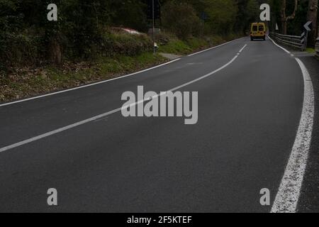 Der Schulbus fährt auf einer zweiweg asphaltierten Bergstraße ab Stockfoto