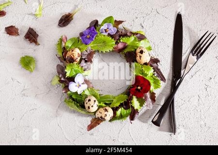 Kranz aus Salatblättern, Blumen und Eiern von oben. Frühlingskomposition mit köstlichen Salat, gesunde Ernährung Ernährung Ernährung Ernährung Lebensmittel zu veranschaulichen. Stockfoto