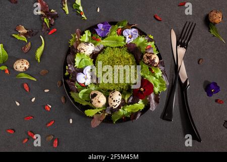 Kranz aus Salatblättern, Blumen und Wachteleiern von oben. Frühlingskomposition mit köstlichen Salat, gesunde Ernährung Ernährung Ernährung Ernährung Lebensmittel zu veranschaulichen. Stockfoto