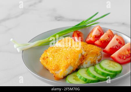 Gebratene panierte Fischfilets mit Gurkenamanttomaten, die aus nächster Nähe auf einem Teller serviert werden. Stockfoto