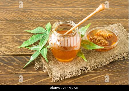 Cannabisblätter, Marihuana und frischer reiner Bio-Honig im Glas auf Holztisch Hintergrund. Honey CBD-Konzept Stockfoto