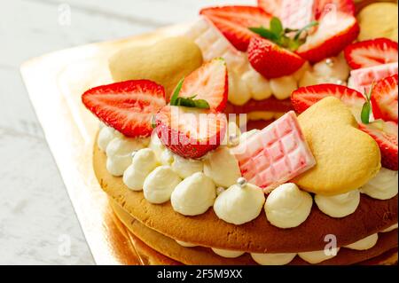 Biskuitkuchen mit Erdbeeren, rosa Milchschokolade, Silberstreuseln, Vanillecreme und herzkranken Keksen aus nächster Nähe. Sommer süßes Dessert für bi Stockfoto