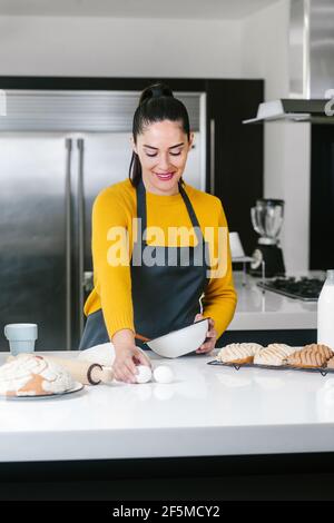 Lateinische Frau steht in der Küche und knetet Teig zu backen Conchas traditionelles mexikanisches Brot Stockfoto