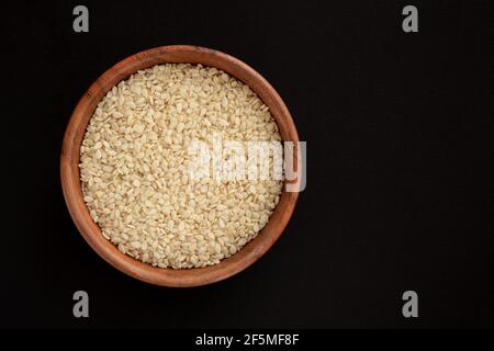 Weiße Sesamsamen in einer Schüssel, isoliert auf schwarzem Hintergrund. Draufsicht. Nahaufnahme. Stockfoto