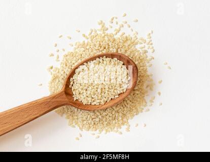 Weiße Sesamsamen in Holzlöffel auf Haufen weißer Sesamsamen, Draufsicht. Stockfoto