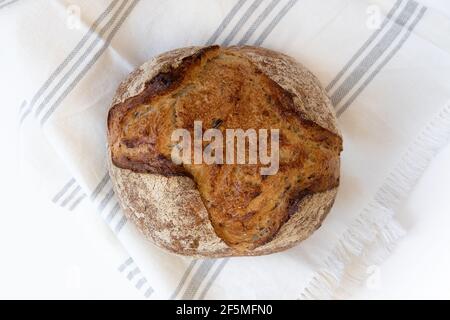 Hausgemachtes Brot. Frisch gebackenes rundes Brot aus Sauerteig mit Leinentuch, Vorderansicht horizontal. Stockfoto