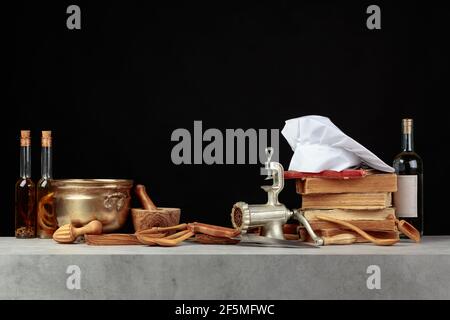 Kochmütze, alte Kochbücher und alte Küchenutensilien auf dem Küchentisch. Speicherplatz kopieren. Schwarzer Hintergrund. Stockfoto