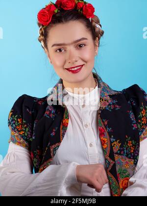 Junge Frau im Bild der mexikanischen Künstlerin Frida mit roten Rosen im Haar. Porträt auf blauem Hintergrund. Stockfoto