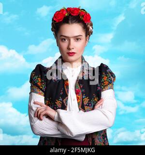 Junge Frau im Bild der mexikanischen Künstlerin Frida mit roten Rosen im Haar. Surrealer Hintergrund mit Himmel. Stockfoto