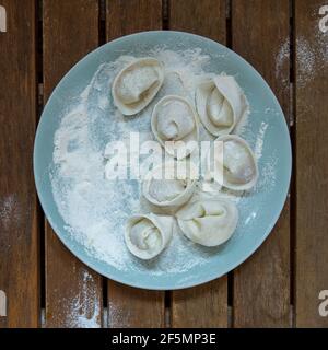 Rohe handgemachte Knödel mit Mehl auf einem hellblauen Teller auf einem dunklen Holztisch. Stockfoto