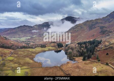 Epische Luftdrohne Landschaftsbild von Blea und Tal in Winter mit niedrigen Wolken und Nebel wirbeln herum Stockfoto