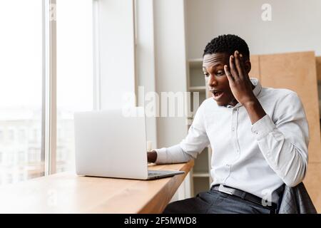 Afro-amerikaner schockiert Mann zum Ausdruck Überraschung während der Arbeit mit Laptop Im Büro Stockfoto