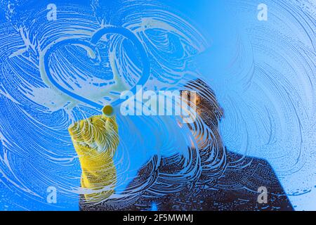 Fensterputzer oder Unterlegscheibe in gelben Handschuhen, die Herzform auf ein Fensterglas zeichnen. Liebe Herz Symbol auf Glas gezeichnet. Konzept der Fensterreinigung Stockfoto