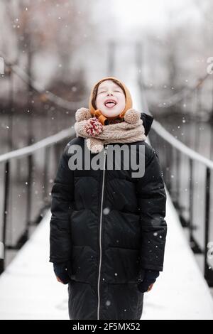 Lustige kleine Mädchen fängt Schneeflocken in einem schönen Winter Park während eines Schneefalls. Niedliches Baby spielt im Schnee. Winteraktivitäten für Kinder. t Stockfoto