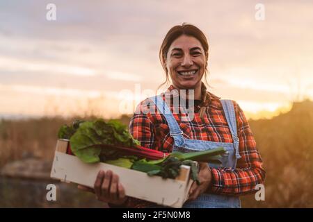 Glückliche Bäuerin mit einer Holzkiste mit frischem Gemüse Stockfoto