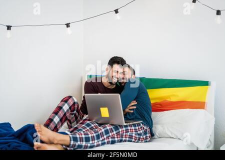 Glücklich Gay paar mit Spaß liegen mit Laptop im Bett - homosexuelle Liebe und Geschlechtergleichstellung in Beziehungskonzept Stockfoto