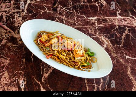 Nudeln mit Gemüse und Garnelen unter Rühren in weißen Keramikschalen anbraten. Schieferhintergrund. Nahaufnahme. Auf Marmorboden. Stockfoto