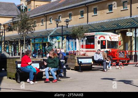 Hastings, East Sussex, Großbritannien. März 2021, 27. UK Wetter: Menschen sitzen auf Bänken genießen die Sonne im Priorat Wiese Einkaufszentrum, Queens Square. Foto-Kredit: Paul Lawrenson /Alamy Live Nachrichten Stockfoto