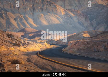 Dramatisches goldenes Licht auf einer leeren gewundenen Wüstenstraße durch das raue Gelände der Badlands-Landschaft im Death Valley Park National Park, USA. Stockfoto