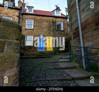 Bunte Eingangstüren auf alten Steinhütten in einer gepflasterten Straße im Küstendorf Robin Hood's Bay in North Yorkshire, Großbritannien. Stockfoto