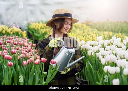 Glücklich lächelnd Teenager Mädchen im Hut mit Gießkanne in Blühender Tulpengarten Stockfoto