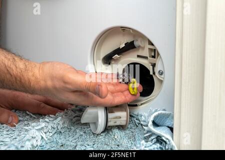 Der Master entfernt den Schmutz aus dem Filter der Waschmaschine. Problem mit dem Wäschewaschen. Stockfoto