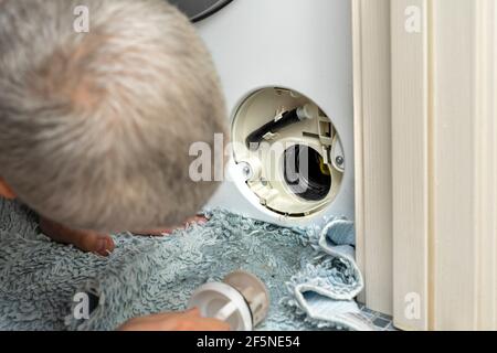 Der Meister schaut in den offenen Filter der Waschmaschine. Waschmaschine verstopft Stockfoto