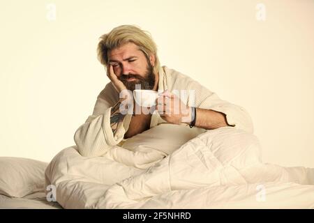 Schöner Mann trinkt Kaffee. Reifer bärtiger Mann im Bett. Der Körper wurde von wesentlichen Komponenten für eine gute Gesundheit und Energie beraubt. Start Tag mit gut Stockfoto