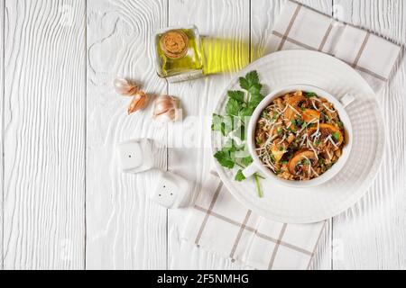 Klassisches cremiges Pilzrisotto mit geriebenem Parmesan und Petersilie in einer weißen Schüssel, Nahaufnahme, italienische Küche, flaches Lay Stockfoto