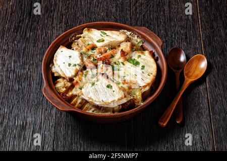Tartiflette, French Potato, Bacon und Käse Auflauf in einer Tonschale auf einem dunklen Holztisch mit Löffeln, französische Küche Stockfoto