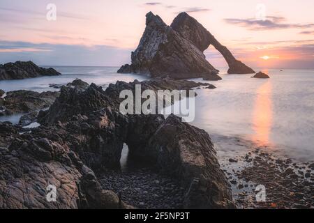 Wunderschöne dramatische Landschaft bei Sonnenaufgang oder Sonnenuntergang des Bow Fiddle Rock Meeresbogens am felsigen Ufer von Portknockie am Moray Firth in Schottland. Stockfoto