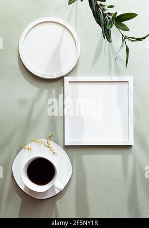 Weiße leere runde und quadratische Fotorahmen und weiße Tasse schwarzen Kaffee auf einem grünen pastellfarbenen Hintergrund. Postermockup mit romantischen langen Schatten. Stockfoto